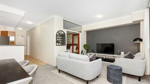 A modern living room with a sofa set, a coffee table, a TV, and a dining area with a table and chairs. - Executive Elegance: Stylish 1BR Suite on Hay St (East Perth)
