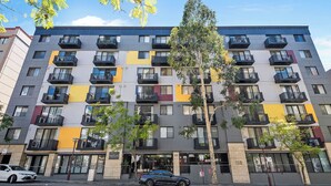 A multi-story apartment building with balconies, a visible storefront, and a parked car. - Executive Elegance: Stylish 1BR Suite on Hay St (East Perth)