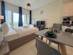 Et moderne hotelværelse med seng, skrivebord, spisebord, tv og vaskemaskine, samt udsigt over byen.