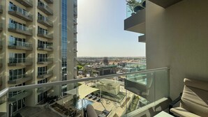 A balcony with a view of a cityscape, a pool, and a building with multiple balconies. - Modern Studio in Virdis Damac Hills 2 (Dubai)