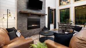A modern living room with a fireplace, leather sofas, and a dining area with natural light from large windows. - Office Desk, Deck, Hot Tub, Fire Pit, Pets, Lost in Nature (Broken Bow)