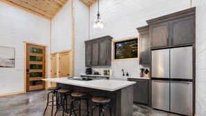 A modern kitchen with a large island, bar stools, a stainless steel refrigerator, and wooden cabinets. - Office Desk, Deck, Hot Tub, Fire Pit, Pets, Lost in Nature (Broken Bow)