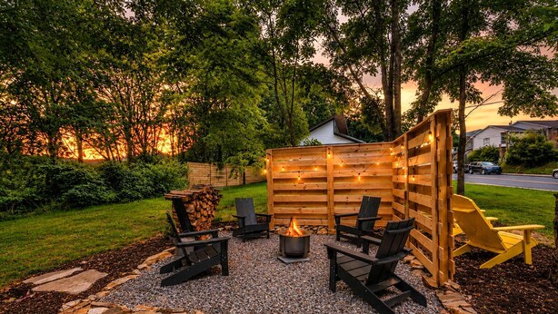 A backyard with a fire pit, seating, and a wooden fence. - Steps Away Cottage • Hot Tub, Fire Pit, Downtown (Waynesville)