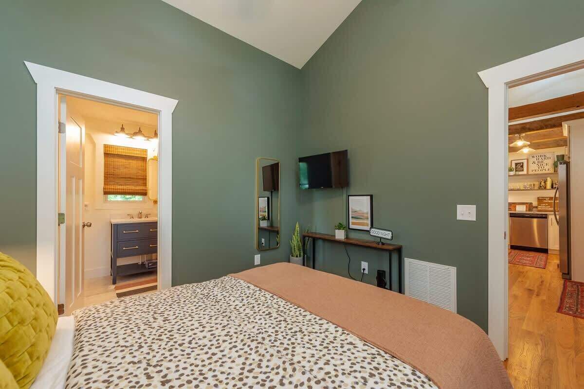 Une chambre à coucher avec un lit, une commode, un miroir, une télévision et une petite table sur laquelle est posée une plante.