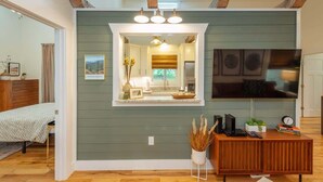A modern living room with a large TV, wooden furniture, and a mirror above the fireplace. - Steps Away Cottage • Hot Tub, Fire Pit, Downtown (Waynesville)