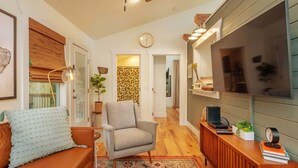 A living room with a sofa, armchair, TV, and a desk with a laptop. - Steps Away Cottage • Hot Tub, Fire Pit, Downtown (Waynesville)