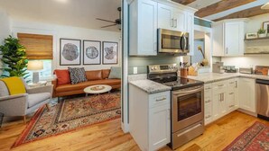 A modern kitchen with white cabinets, stainless steel appliances, and a wooden ceiling. - Steps Away Cottage • Hot Tub, Fire Pit, Downtown (Waynesville)