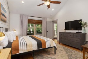 A bedroom with a bed, a ceiling fan, a TV, a dresser, and a window with curtains. - Birdsong Cottage | Gorgeous Lake Junaluska Retreat (Waynesville)