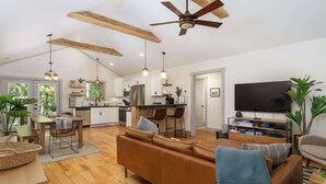A spacious living area with a brown sofa, wooden ceiling beams, and a ceiling fan. - Birdsong Cottage | Gorgeous Lake Junaluska Retreat (Waynesville)