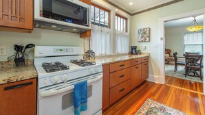 A kitchen with wooden cabinets, a gas stove, a microwave, and a large window with curtains. - Bohemian Paradise | Near Downtown | Monthly Stays! (Asheville)