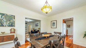 A dining area with a wooden table, chairs, and a chandelier. There is a painting on the wall and a cabinet with decorative items. - Bohemian Paradise | Near Downtown | Monthly Stays! (Asheville)