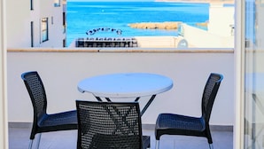 A balcony with a round table and two chairs, overlooking a coastal view with a clear sky and calm sea. - Fenix Apartments (Bar)