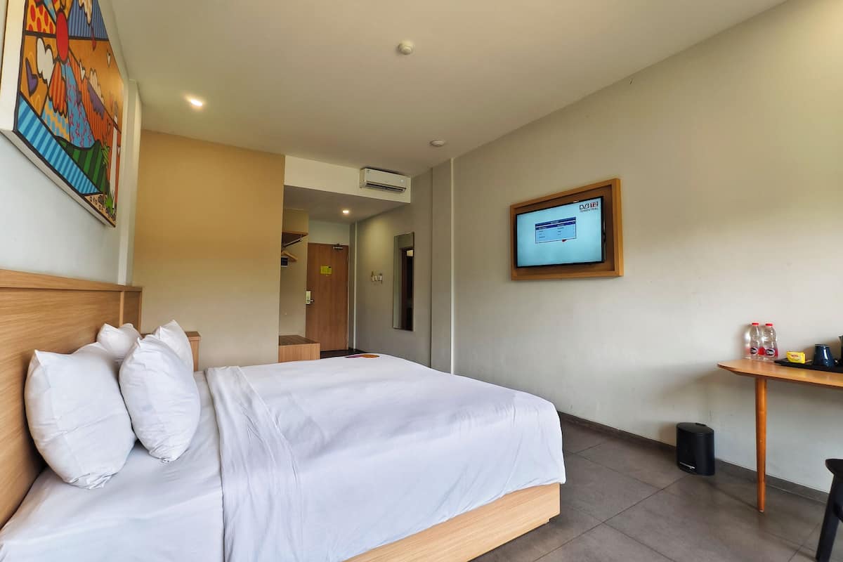 A hotel room with a bed, a TV mounted on the wall, and a small table with a trash bin.