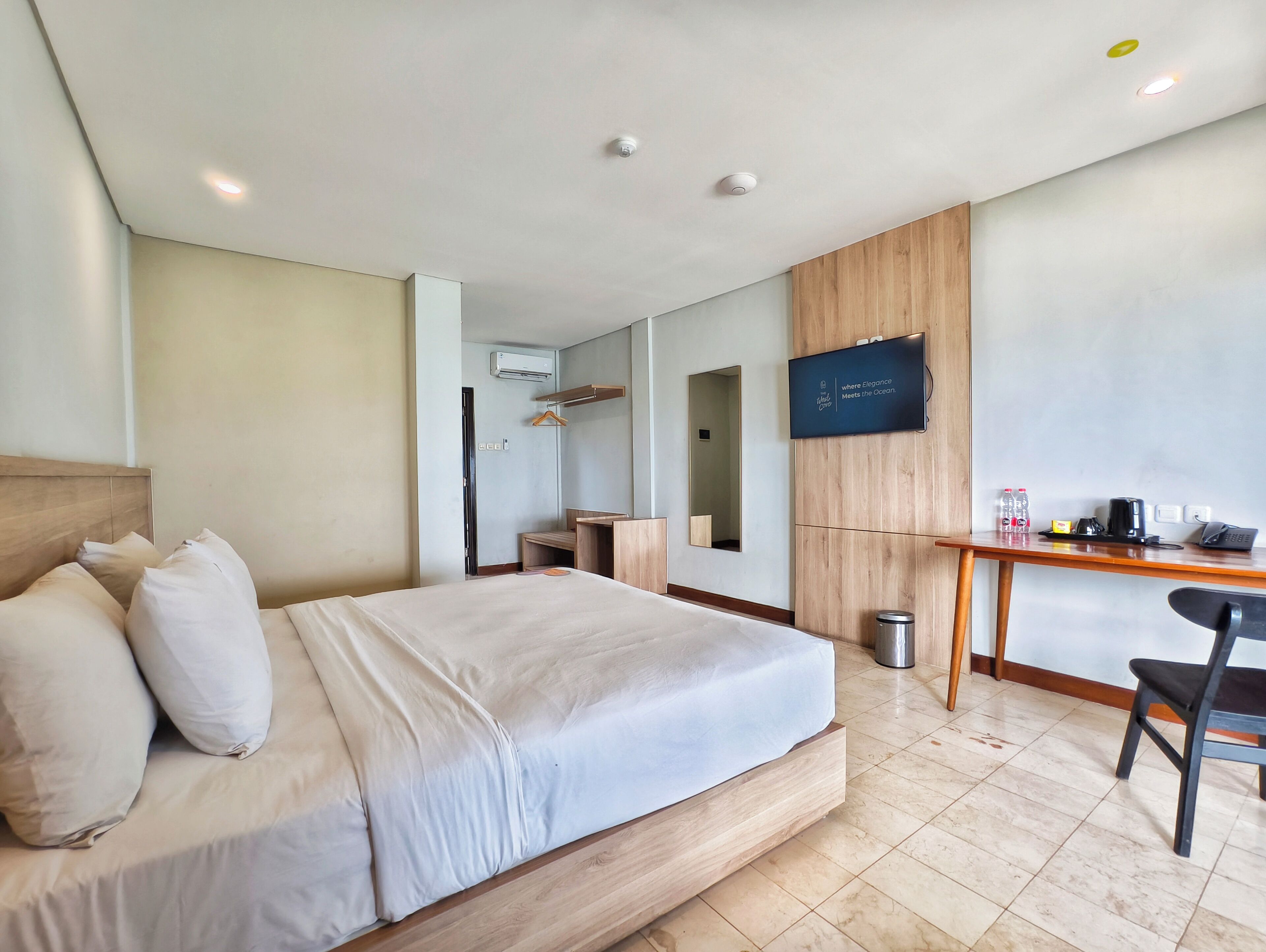 Quarto de hotel com cama, escrivaninha, cadeira, televisão e espelho.