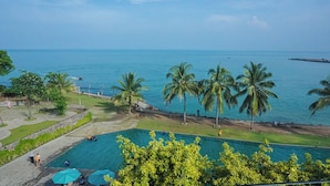 A pool area with a view of the sea, palm trees, and a stone pathway.