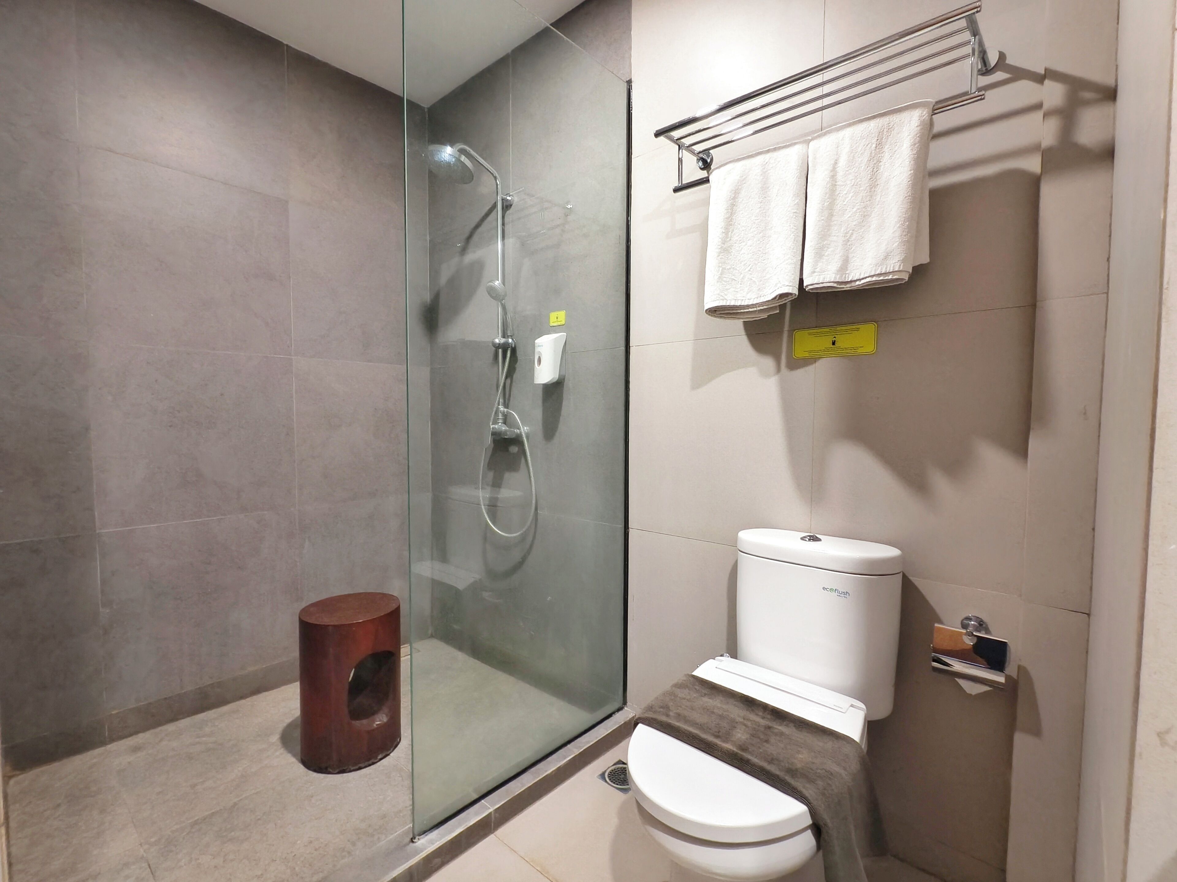 Un baño moderno con ducha envuelta en vidrio, inodoro con toallero superior y un pequeño cubo de basura.