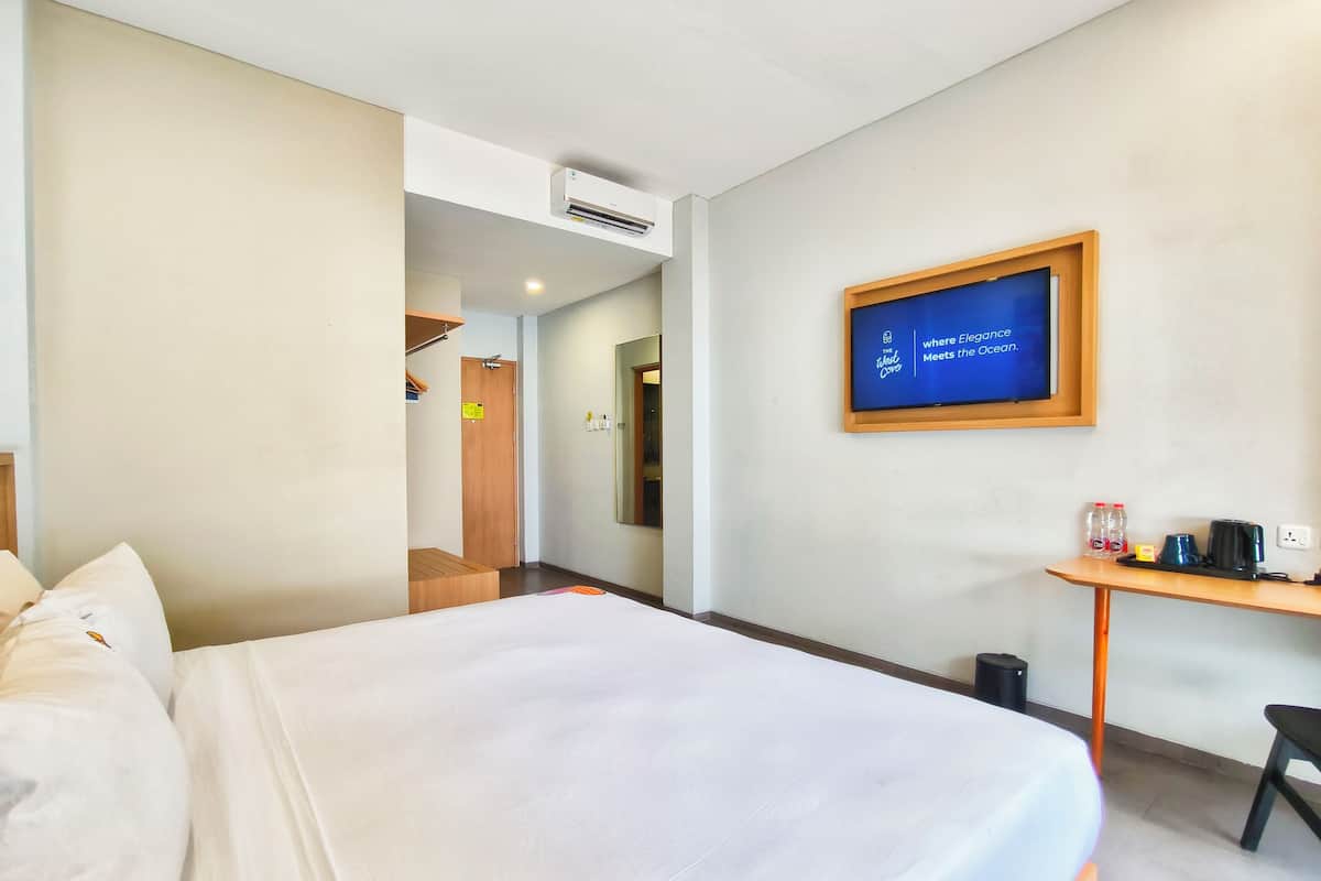 A hotel room with a bed, a desk with a coffee maker, a TV screen, and an air conditioning unit.