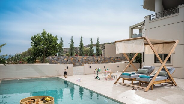 A pool area with lounge chairs, a table with a basket of fruits, and a view of the surrounding landscape.