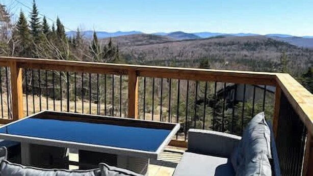 Eine Terrasse mit Gartenmöbeln, darunter ein Tisch und gepolsterte Sitzgelegenheiten, mit Blick auf eine Berglandschaft.