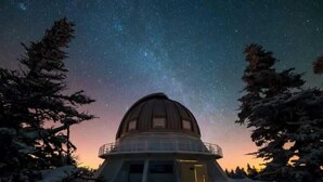 Ein kuppelbedecktes Observatorium, umgeben von schneebedeckten Bäumen, unter einem sternenübersäten Nachthimmel.