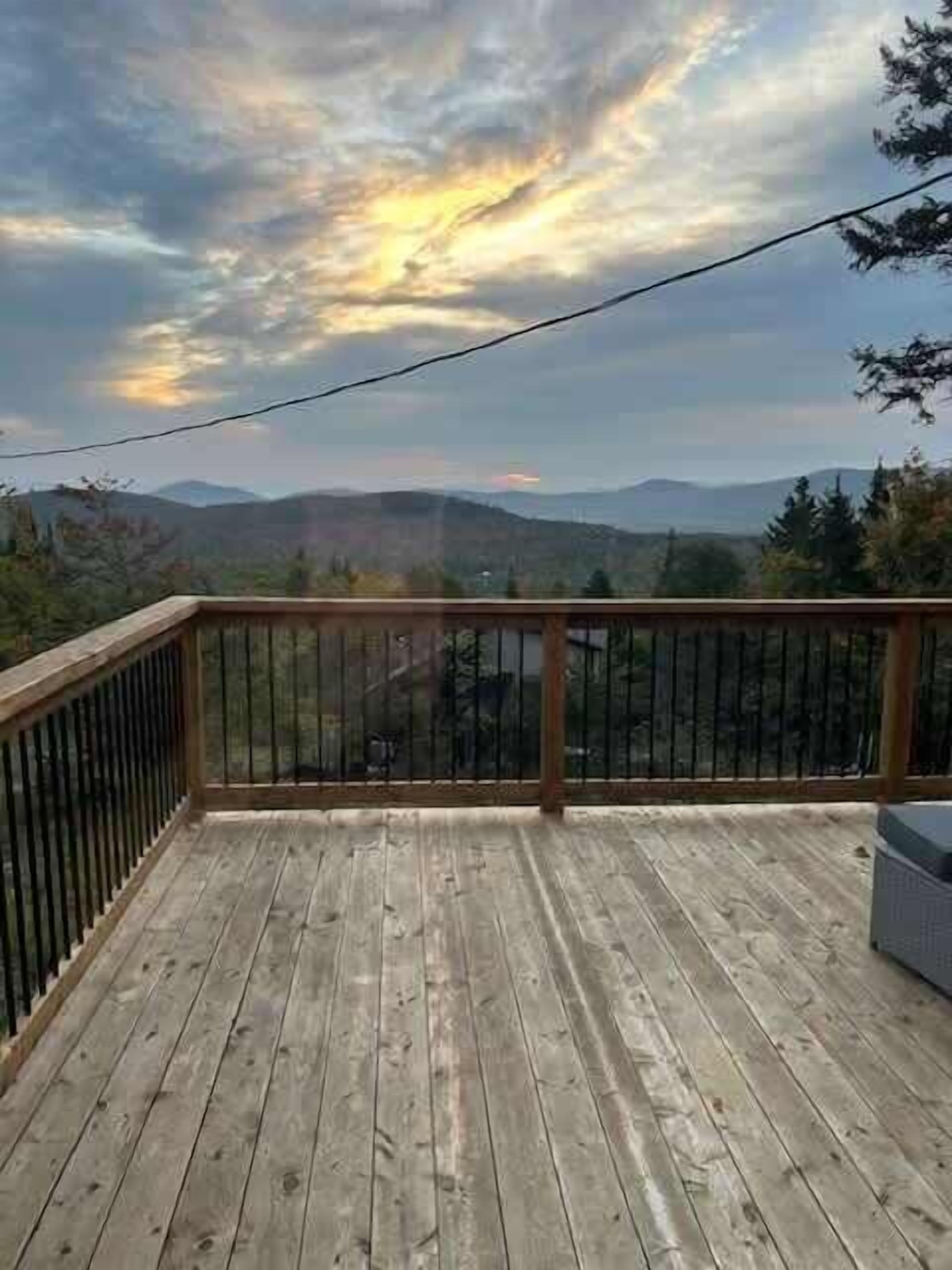 A wooden deck with a metal railing, overlooking a mountainous landscape.