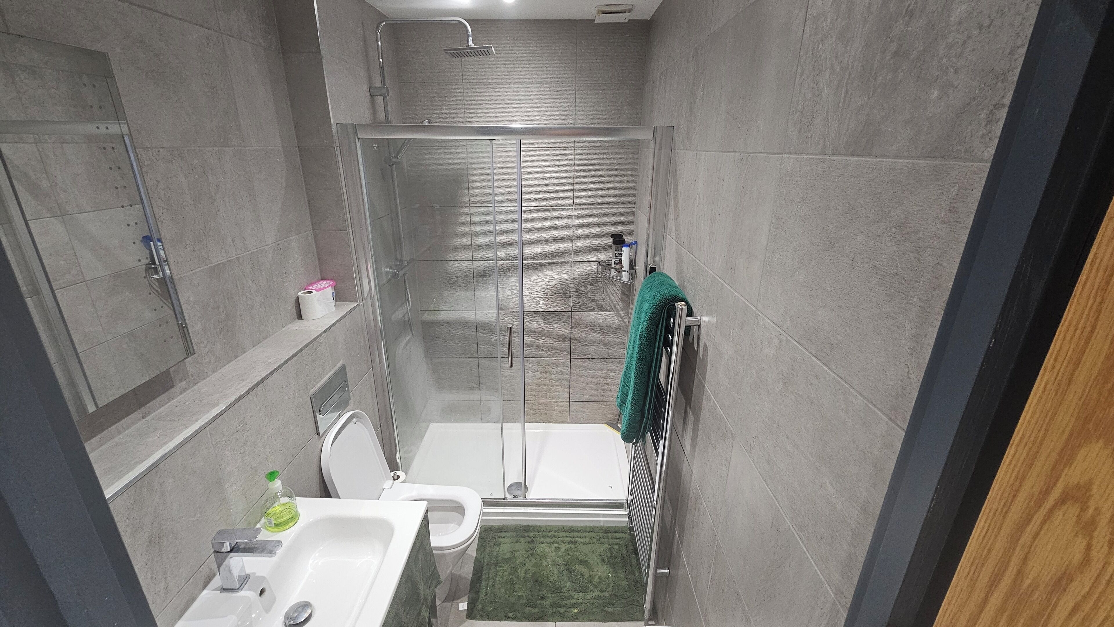 Un bagno moderno con cabina doccia in vetro, un water, un lavandino e un porta asciugamani.