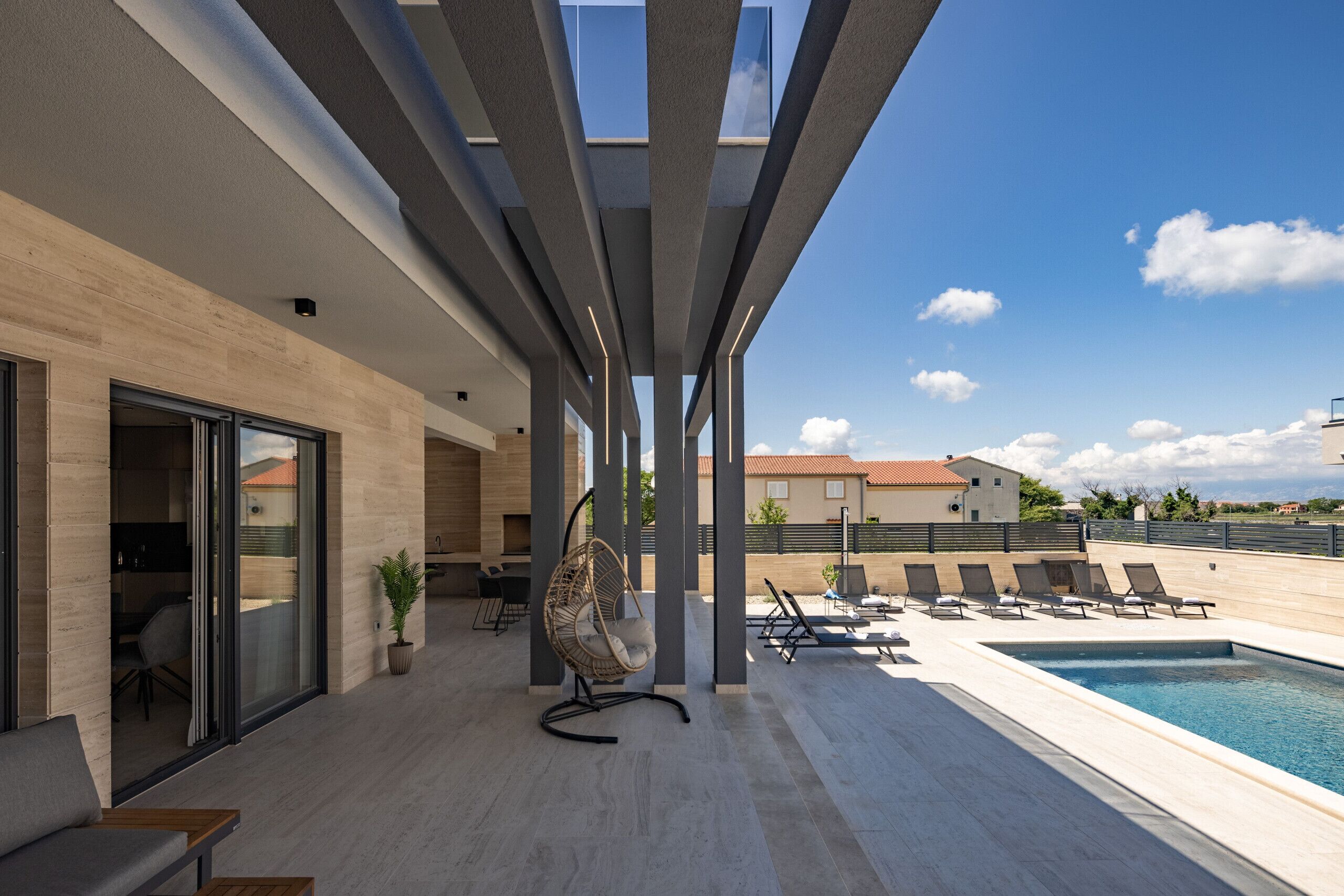 A modern outdoor pool area with a seating area, a hanging chair, and a view of the surrounding buildings.