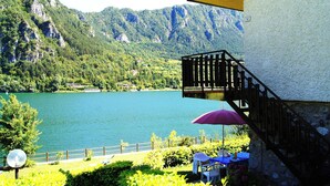 A balcony with a view of a lake and mountains, a wooden fence, and a table with a chair. - Direkt am See mit Terrasse (Tre Capitelli)