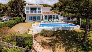 Une maison à deux étages avec une piscine, entourée de verdure et d’arbres.