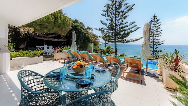 Une terrasse extérieure avec une table en verre, des chaises et une vue sur la mer.