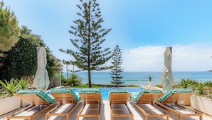 Un espace aménagé au bord de la piscine, avec des chaises longues en bois et une vue sur l’océan.