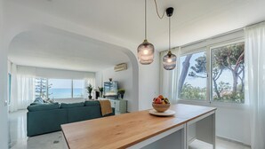 Un salon moderne avec un îlot central en bois, un canapé vert et une vue sur la mer.