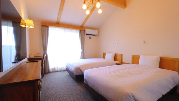 Habitación de hotel con dos camas, un escritorio, un espejo y una ventana con cortinas.