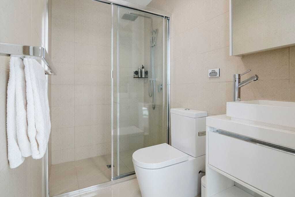 A modern bathroom with a glass-enclosed shower, a white toilet, and a sink with a mirror above it.