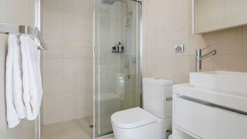 A modern bathroom with a glass-enclosed shower, a white toilet, and a sink with a mirror above it.