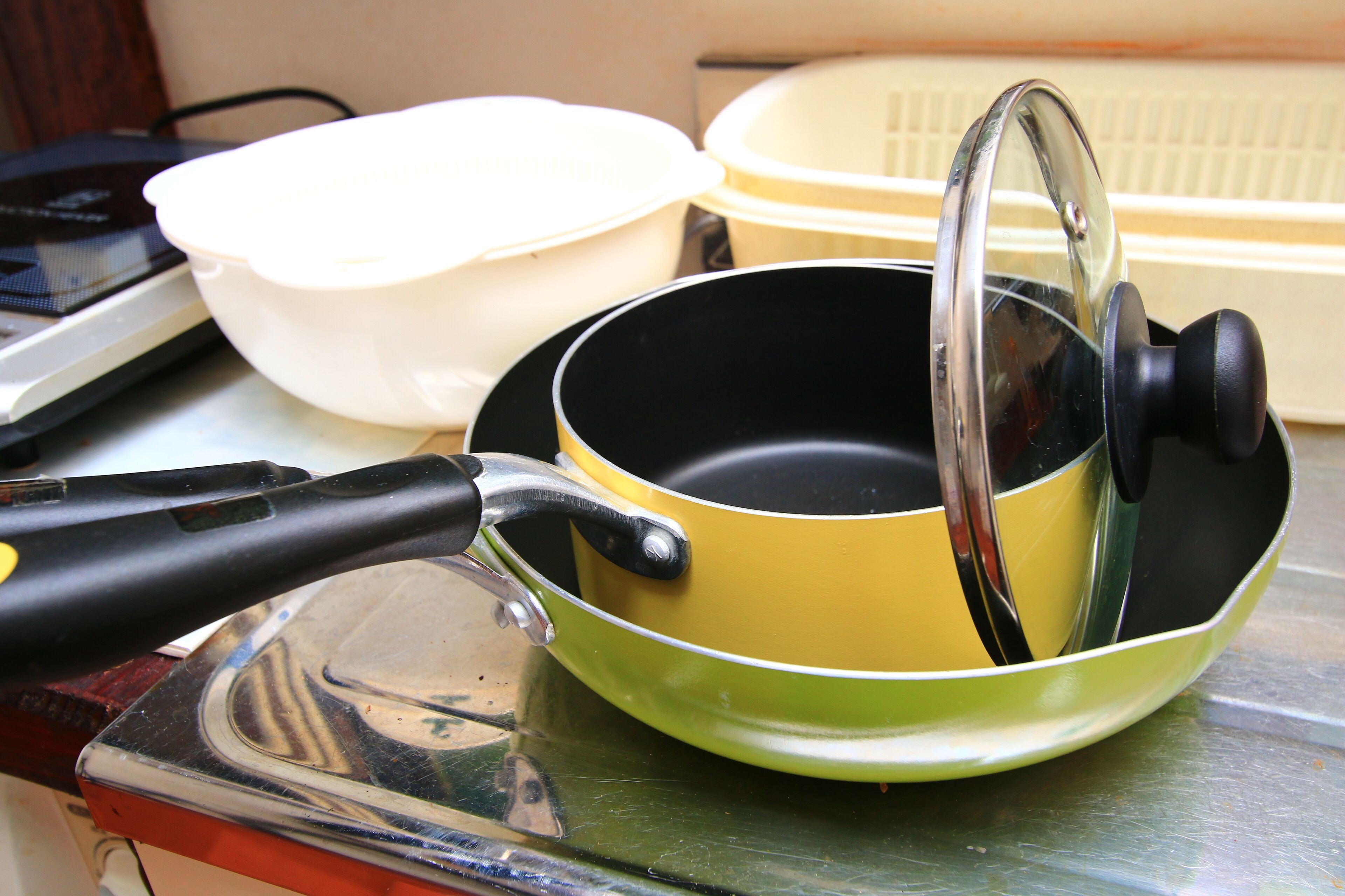 A kitchen counter with a green frying pan, a white bowl, and a plastic container.