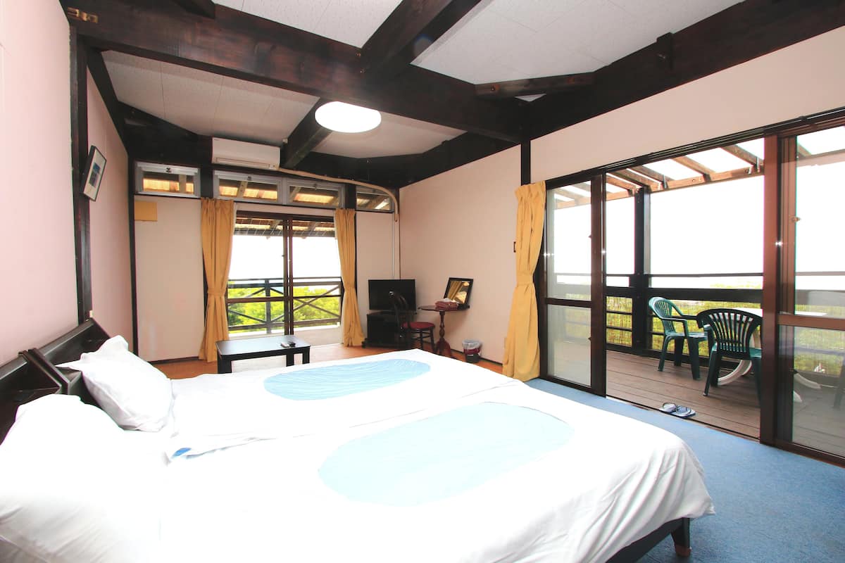 Une chambre avec un grand lit, un bureau et une chaise, une télévision et un balcon équipé de chaises.
