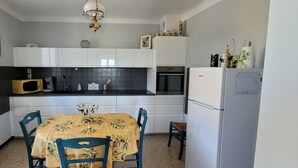 Une cuisine compacte avec des meubles blancs, un four à micro-ondes, un four et un réfrigérateur. On y trouve une table à manger avec des chaises et un saladier décoratif posé dessus.
