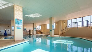 An indoor swimming pool with clear water, a pool rule sign, and a staircase leading to a balcony. - Beautifully Decorated Direct Oceanfront 2 Bedroom Condo (Ocean City)
