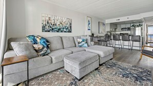 A modern living room with a grey sectional sofa, a small wooden side table, and a patterned rug. - Beautifully Decorated Direct Oceanfront 2 Bedroom Condo (Ocean City)