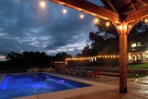 Un espace piscine agrémenté d’une pergola en bois et de guirlandes lumineuses, entouré de chaises longues.