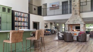 A spacious living area with a stone fireplace, high ceilings, and a balcony with artwork. - Luxury in Wimberley | Pool+Pickleball+Party Barn (Wimberley)
