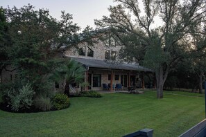 Une maison en pierre dotée d’un patio couvert, entourée d’une végétation luxuriante et d’arbres.
