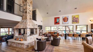 A spacious living area with a stone fireplace, leather seating, and large windows offering views of the outdoors. - Luxury in Wimberley | Pool+Pickleball+Party Barn (Wimberley)