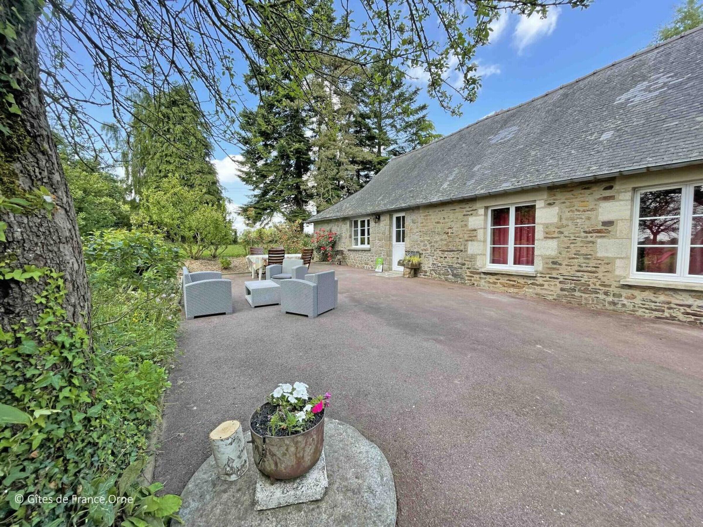 Un bâtiment en pierre avec une allée pavée et un espace extérieur aménagé pour s’asseoir.