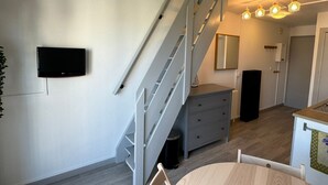 Een modern interieur met een trap, een flatscreen televisie aan de wand, een klein dressoir en een eethoek met een ronde tafel.