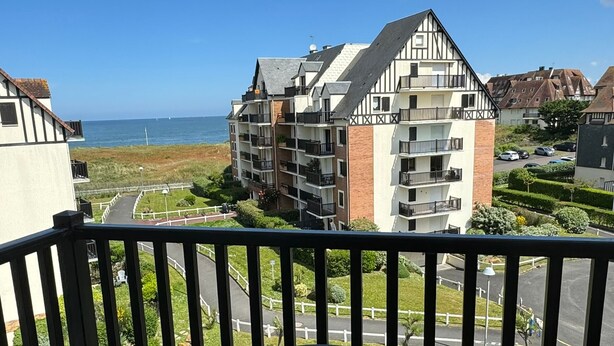 Een balkon met een tafel en stoelen, met uitzicht op een woonwijk en de zee.
