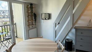 Een moderne woonkamer met een ronde houten tafel, een grijze kast en een aan de muur bevestigde televisie.