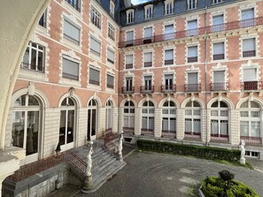 Un immeuble à plusieurs étages doté d’une façade symétrique, avec des fenêtres en arc de cercle et des balcons ornés de rampes rouges.