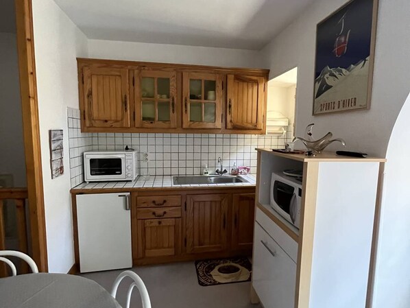 Une cuisine compacte avec des meubles en bois, un four à micro-ondes, un évier et un petit réfrigérateur.